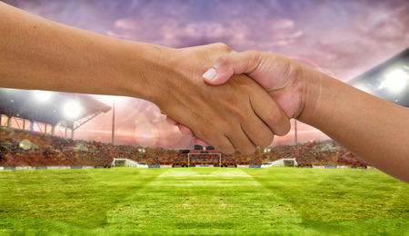 handshake in a business opponent team players shaking hand on football stadium backgroundの写真素材