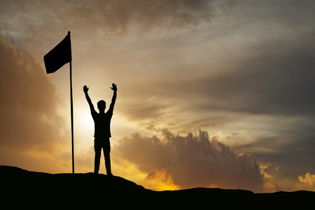 silhouette of man show arm up for achievements successful and celebrating success on sunset and silhouette of businessman with flag on mountainの写真素材