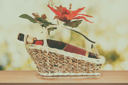 wine bottle with blank label on present basket with fake flower on wooden table nature and green bokeh background For product displayの写真素材