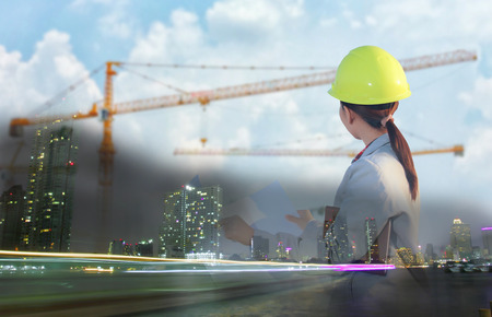 Double exposure women asia engineer working and holding blueprints at construction siteの写真素材