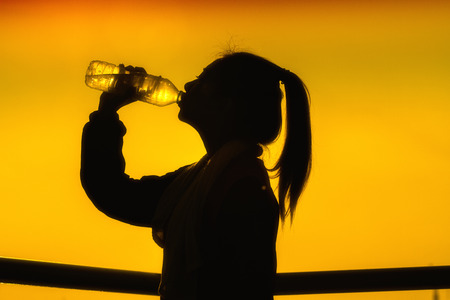 Silhouettes picture of Sporty Asian woman drinking water outdoor and soft focusの写真素材