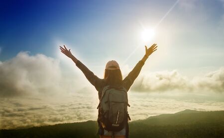 Freedom traveler woman standing with raised arms and enjoying a beautiful nature and cheering young woman backpacker at sunrise seaside mountain peakの写真素材