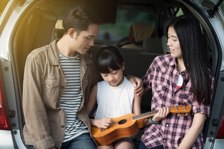 happy little girl playing ukulele with asian family sitting in the car for enjoying road trip and summer vacationの写真素材