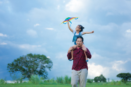 Asian child girl and father with a kite running and happy on meadow in summer in natureの写真素材