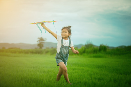 Asian child girl with a kite running and happy on meadow in summer in natureの写真素材