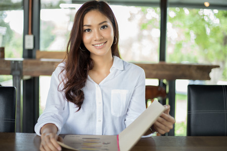 Asian woman open menu for ordering in coffee cafe and restaurant and smiling for happy timeの写真素材