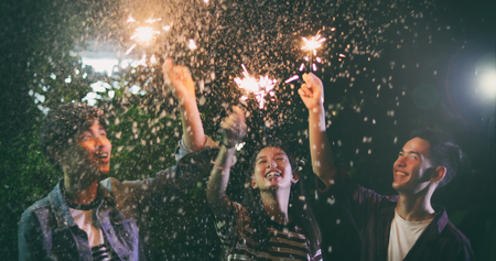 Asian group of friends having outdoor garden barbecue laughing with alcoholic beer drinks and showing group of friends having fun with sparklers on night ,soft focusの写真素材