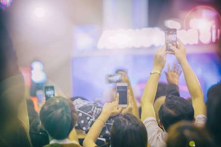 Asian  women holding smart phone and tapping screen for taking pictures on Crowd at concert stage lights,blurry backgroundの写真素材