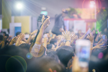 Asian  women holding camera for taking pictures on Crowd at concert stage lights,blurry background