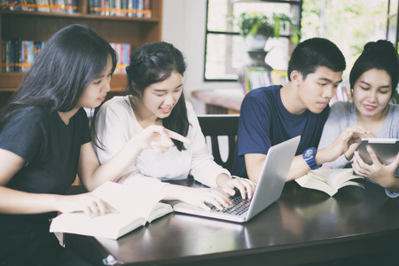 Asian Group of students using tablet and notebook sharing with the ideas for working on the campus lawnの写真素材