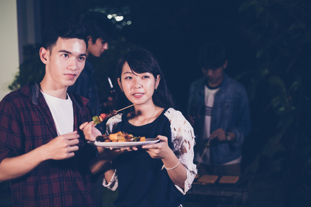 Asian group of friends having outdoor garden barbecue laughing with alcoholic beer drinks on nightの写真素材