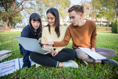 Group Of University Students asian sitting on the green grass  Working and reading Outside Together in a park の写真素材