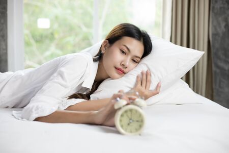 asian woman happy waking up and turning off the alarm clock having a good dayの写真素材
