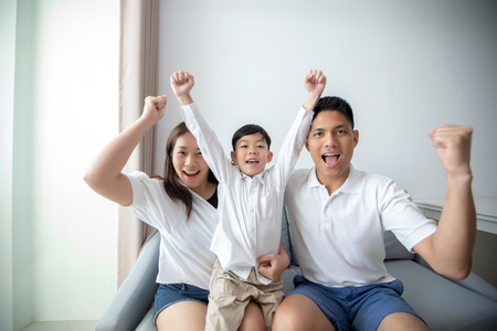 Excited and Happy family with arms raised while watching television at homeの写真素材