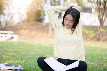 Asian woman stretching and sitting on the green grass after reading book and work hard  in a parkの写真素材