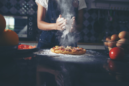 Asian women preparing a pizza, knead the dough and puts ingredients on kitchen tableの写真素材