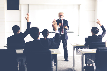 Business Audience raising hand up while businessman is speaking in training for Opinion with Meeting Leader in Conference Roomの写真素材
