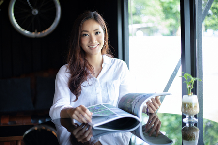 Asian women smiling and reading a book for relaxation at coffee cafeの写真素材