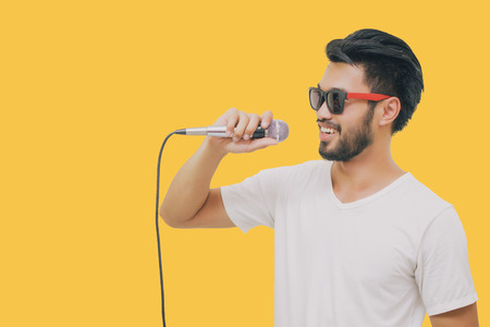 Asian handsome man with a mustache, smiling and singing to the microphone isolated on yellow backgroundの写真素材