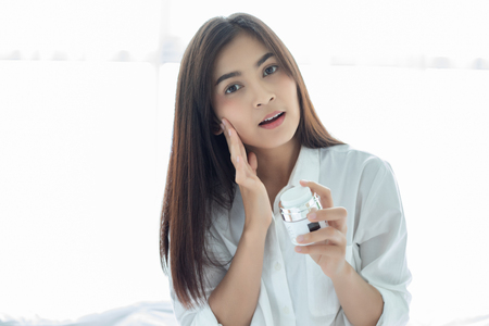 A beautiful woman asian using a skin care product, moisturizer or lotion taking care of her dry complexion. Moisturizing cream in female hands .の写真素材