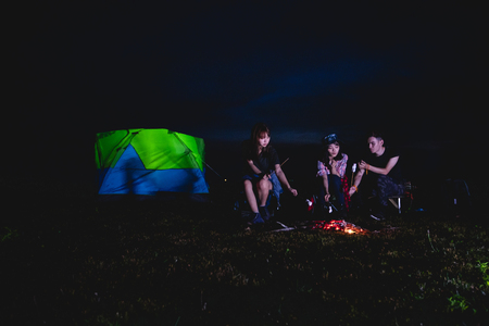 A group of Asian friends tourist drinking and playing guitar together with happiness in Summer while having camping near lakeの写真素材