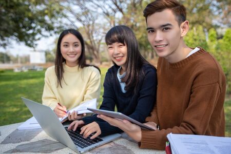 Group Of University Students asian sitting on the green grass  Working and reading Outside Together in a parkの写真素材