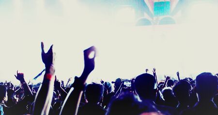 silhouettes of concert crowd at Rear view of festival crowd raising their hands on bright stage...