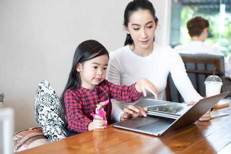 Mom is teaching her daughter to read a book and playing notebook.