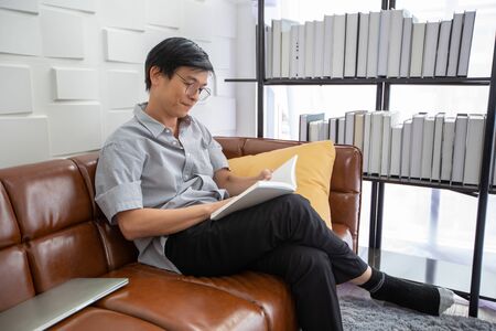 Senior Asian man reading book on sofa in living room at home ,Portrait of Asian elderly man is Relaxing and Happiness With Read a Magazineの写真素材