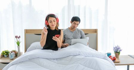 Asian couple lovers listening to music and singing on his bed and happy on relax timeの写真素材