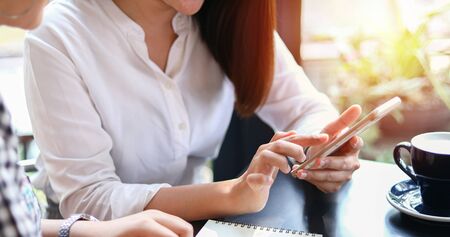 Two Asian women drinking coffee in a cafe and shopping online on smart phonesの写真素材