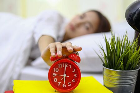Asian woman happy waking up and turning off the alarm clock having a good dayの写真素材