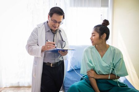 The doctors are asking and explaining about the illness to a female patient lying in bed at a...