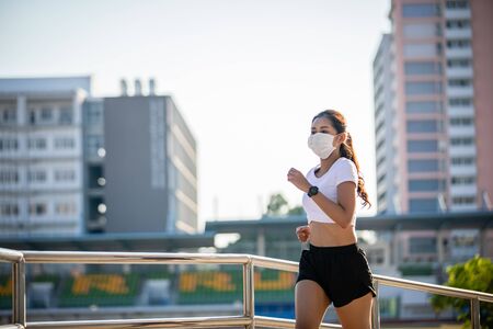 Asian Young fitness sport woman running  and she wears a mask for protective Dust and pollution and protection flu virus, influenza, coronavirus on cityの写真素材