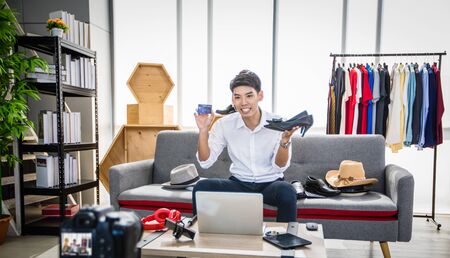 Asian man blogger broadcasting a video for selling product online such as Hats, shoes, headphones, clothing, safety headers.Shopping online concept  at homeの写真素材