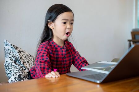 Asian girl or daughters use notebooks and technology for online learning during school holidays and watching cartoons at home. Educational concepts and activities of the familyの写真素材