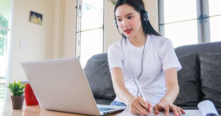 Asian happy woman student wear headphones study online watching webinar podcast on laptop listening...