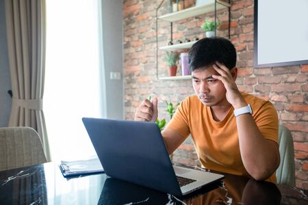 Asian man uses a notebook computer and works hard and meeting at home and he is stressed and...