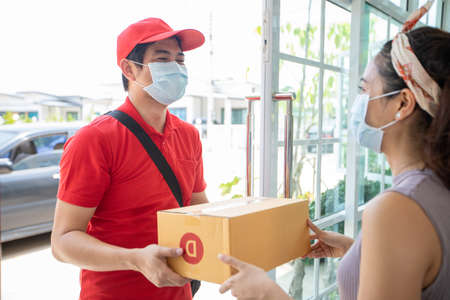Asian delivery servicemen wearing a red uniform with a red cap and face mask handling cardboard...
