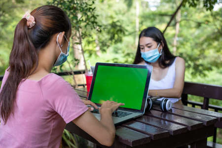 Asian women talking with a friend and holding shopping bag in a shopping mall and they wearing a face mask for protection during coronavirusの写真素材