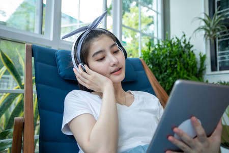 Asian women wearing headphones and using  digital tablet on a relaxing day at home