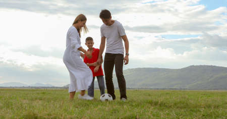 Asian families play football at a meadow near the river on a summer holiday.