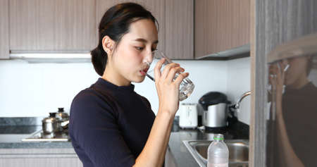 Asian woman drinking water on glass in kitchen