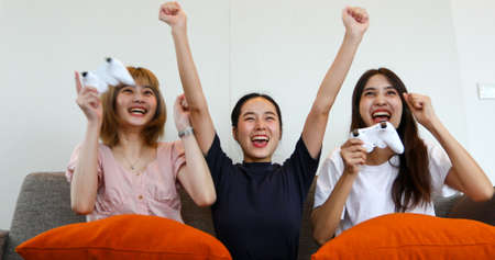 Asian women and friends are playing games and laughing in excitement on the sofa at home.