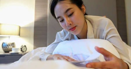 Asian women reading a book and smiling and happy Relaxing in the bedroom at homeの写真素材