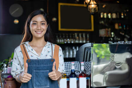 Asian business owner and barista wearing face mask and smiling after reopening coffee shopの写真素材