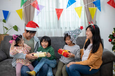 Asian Happy family with daughter in Santa hats gathered together on Christmas time and enjoy gifts boxの写真素材