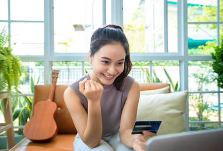 Asian woman is holding credit card and using smartphone shopping online at home. Online shopping  e-commerce  internet banking  spending money  working from home conceptの写真素材