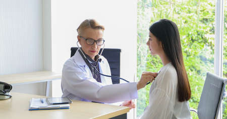 Women doctor used a stethoscope to check the lungs of the woman patient at the hospital.