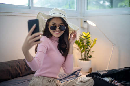 Beautiful Asian women using smartphone selfie and packing suitcases for travelの写真素材
